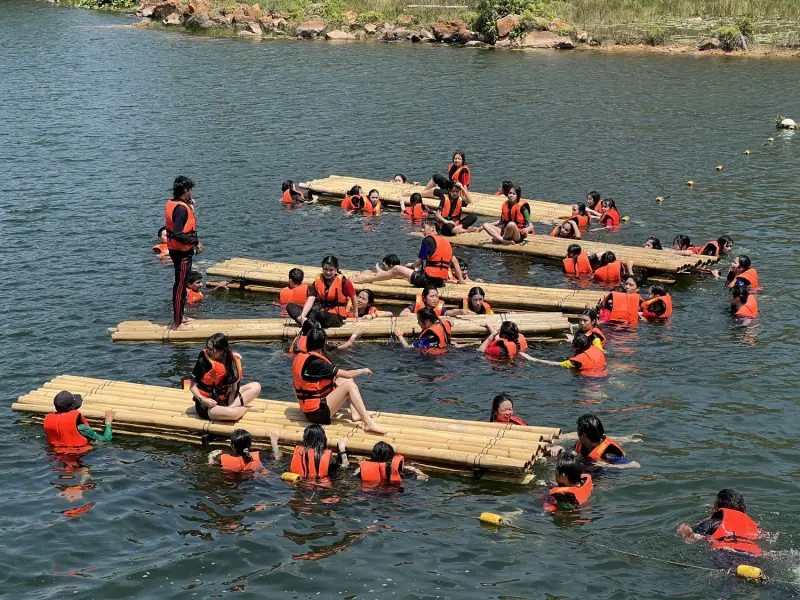 Teams collaborating during an outdoor bamboo raft and lake challenge